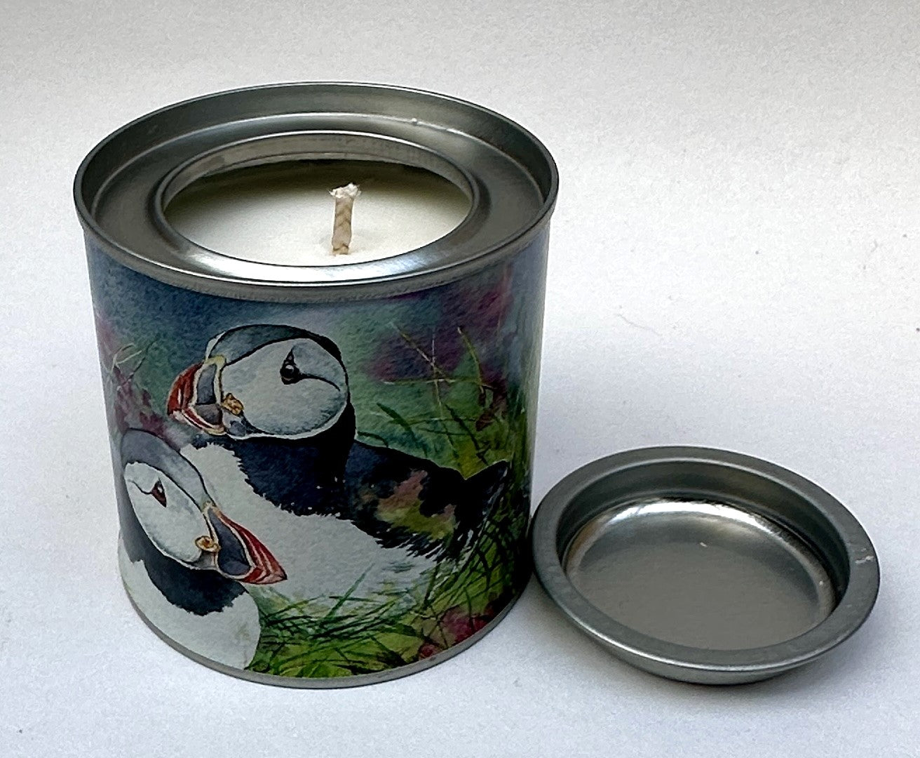 small candle tin with a watercolour picture of puffins sitting in amongst wildflowers and grass