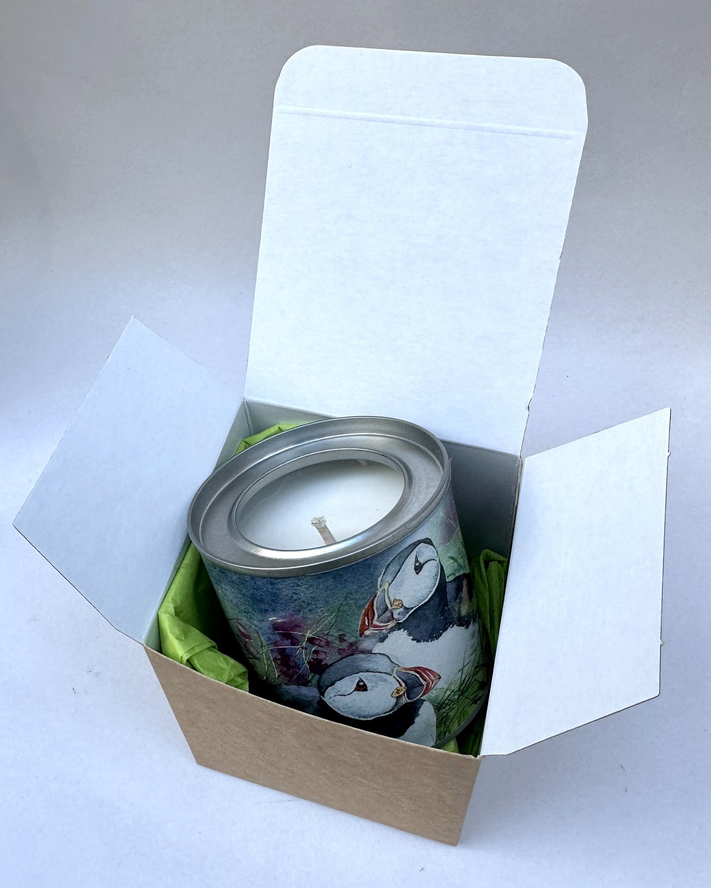 small candle tin with a watercolour picture of puffins sitting in amongst wildflowers and grass