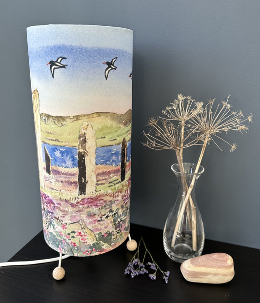 a tall table lamp printed with a watercolour image of The Ring of Brodgar in Orkney with oystercatchers in the sky and curlews below in the purple heather