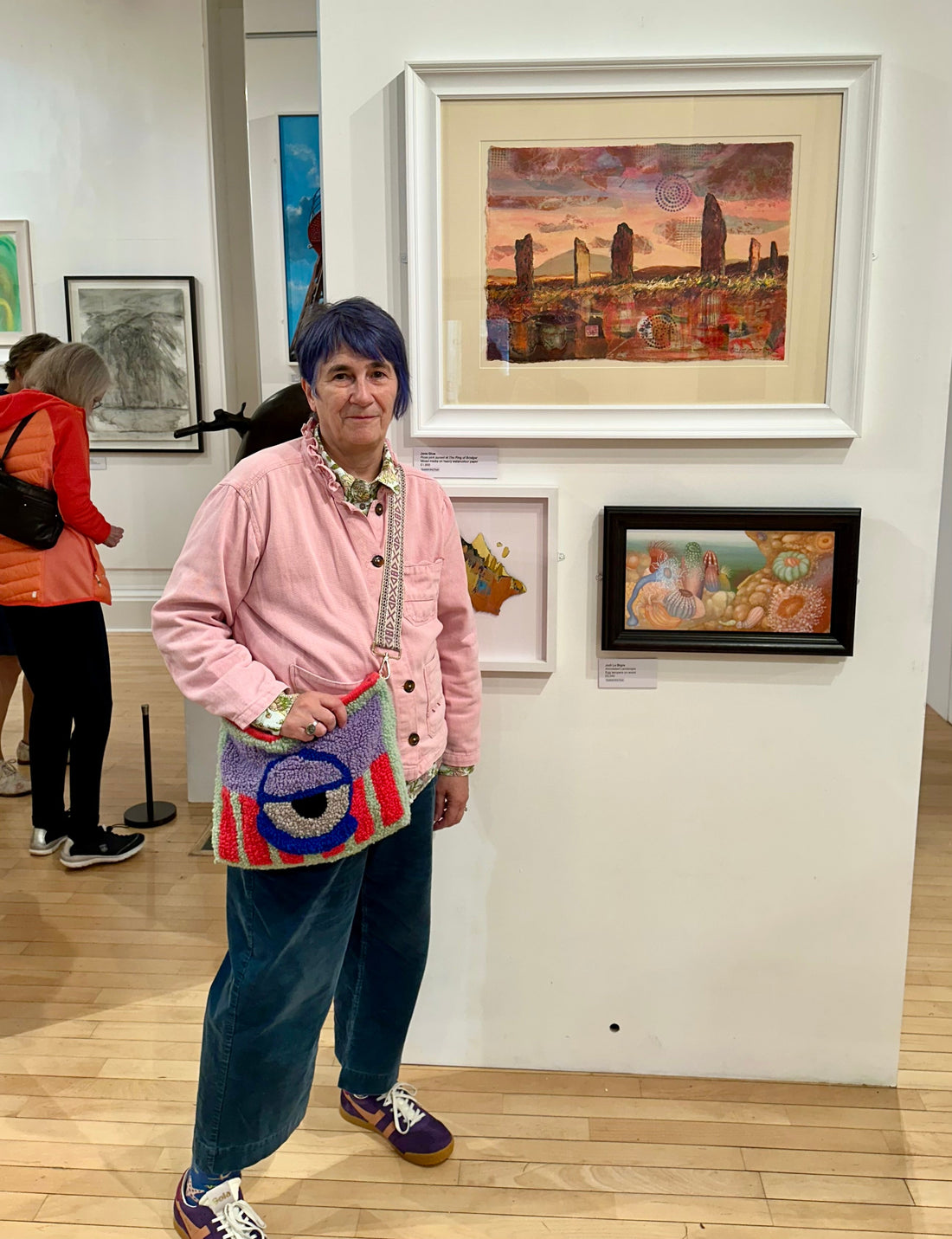 Orkney artist Jane Glue standing in front of her painting 'Rose pink sunset at The Ring of Brodgar' at the Scottish Landscape awards 2025 exhibition at Kirkcudbright galleries.