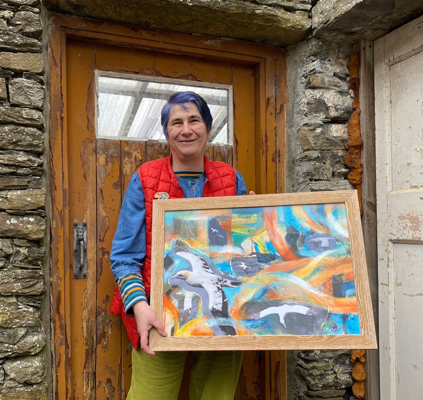 A photograph of Orkney artist Jane Glue holding her original painting of Gannets on a summers day in Orkney, Scotland