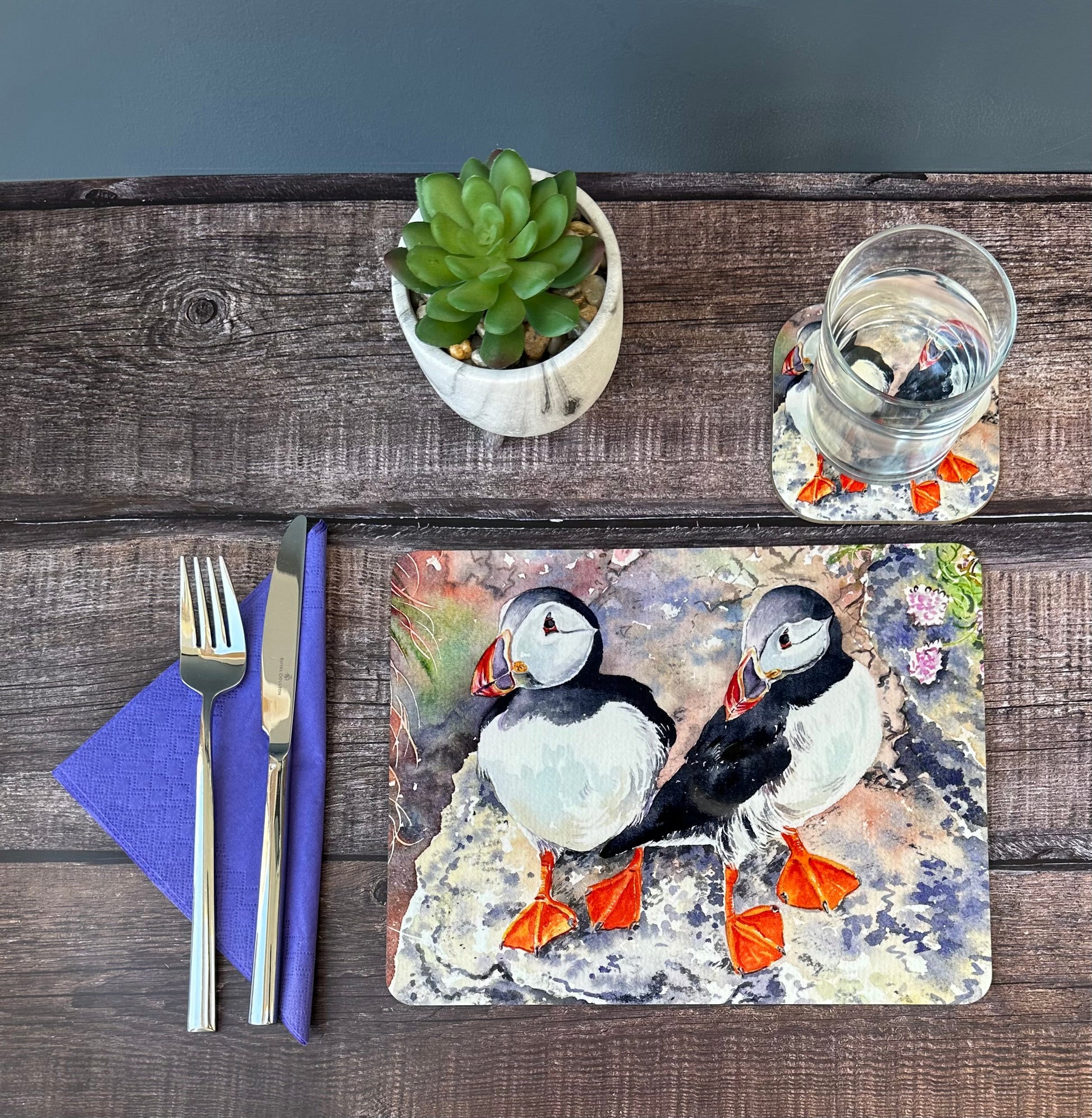 a tablemat and coaster of two orkney puffins on a cliff