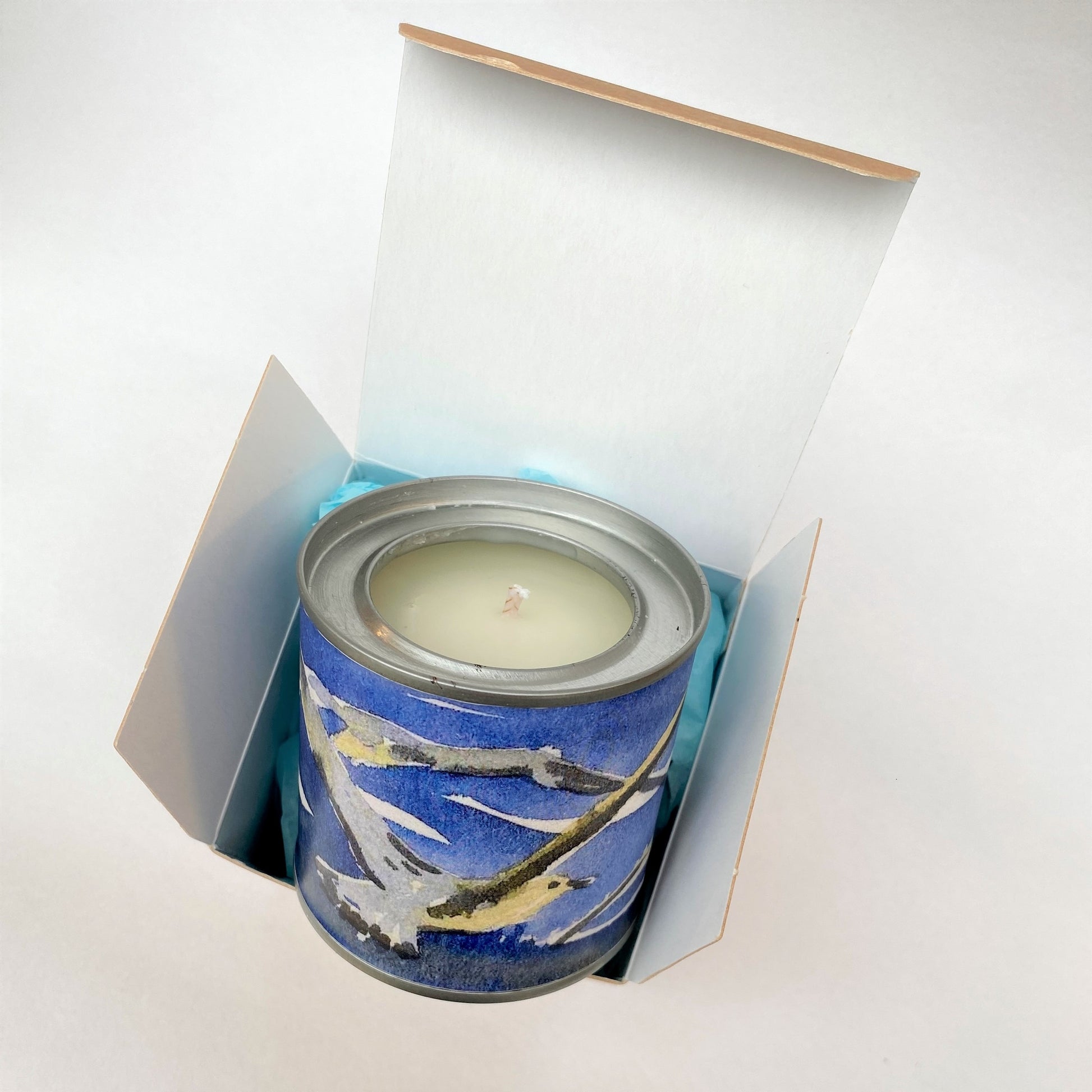 small handmade candle printed with a watercolour picture of gulls against a blue sea